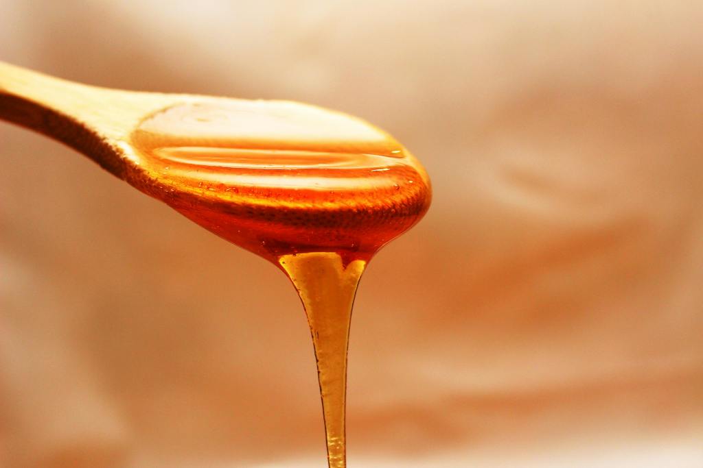 A wooden spoon with golden liquid honey pouring off of it.